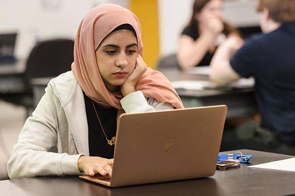 A student wearing a hijab works on a laptop computer in a classroom 