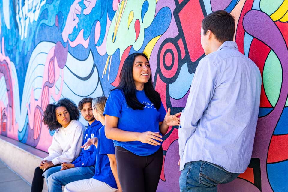 College students converse in front of a colorful mural