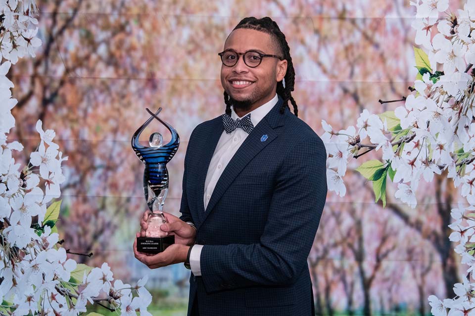 Aric Hamilton poses for a photo with an award in front of a floral background.