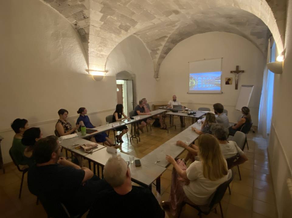 Conference attendees sit in a room with arched ceilings, looking at a video screen.