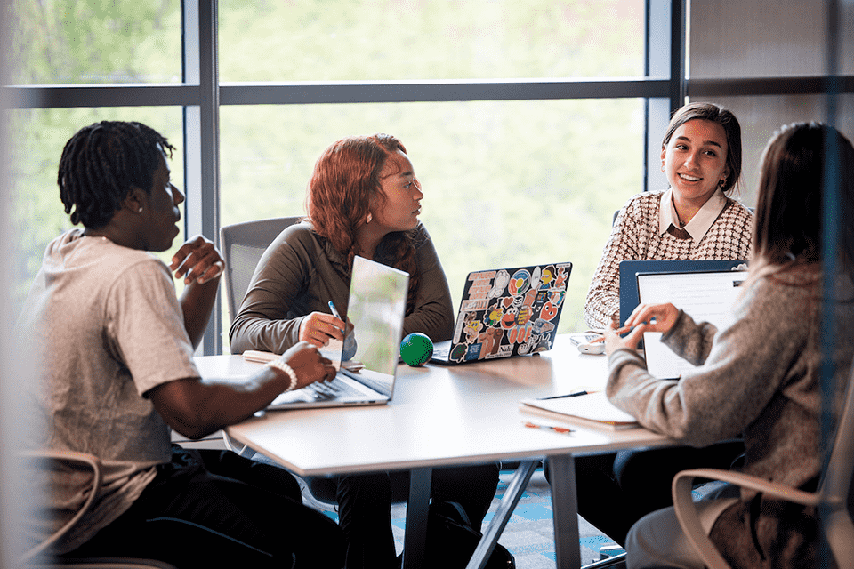 Four students study around a table with laptops in front of them.