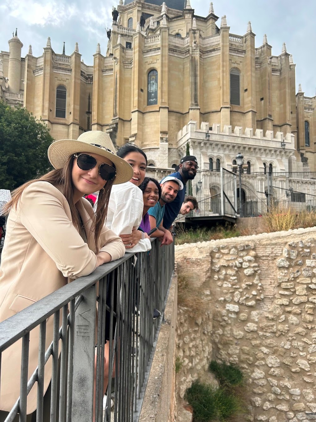 Students look over the railing of a bridge in front of a historic building.