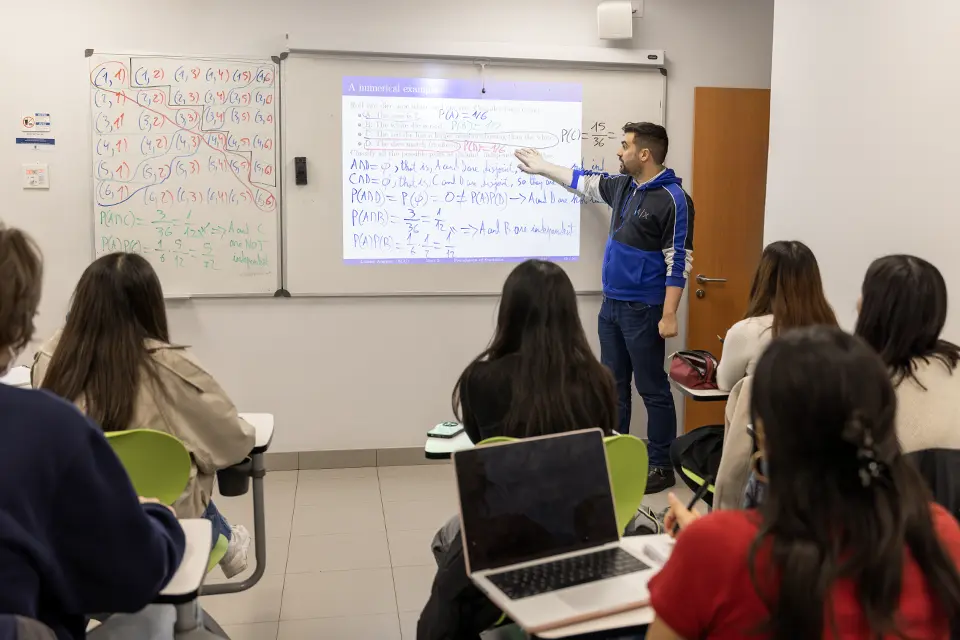 A teacher writing on a blackboard in front of a group of students attending class.