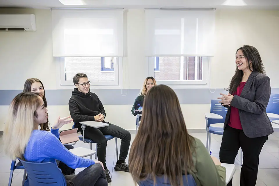 A standing teacher speaking to a group of seated students.