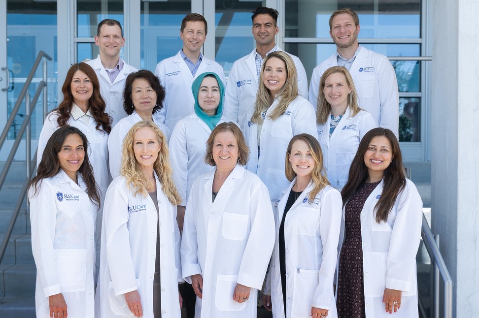 Faculty members wearing white doctors' coats stand in three rows for a group photo.
