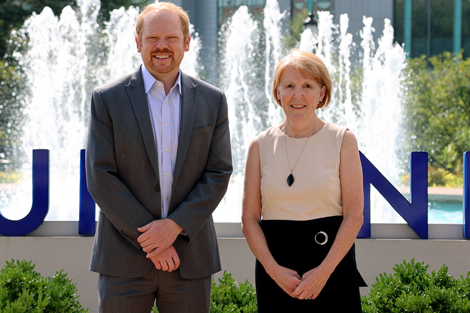 Max Zubatsky, Ph.D., LMFT, left, associate professor in family and community medicine, and Marla Berg-Weger, Ph.D., MSW, right, pose for a photo in front of a fountain on SLU's campus on a bright sunny day.