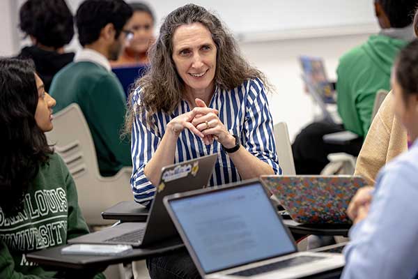 A professor listens and speak intently with students in a classroom while the students do a group project.