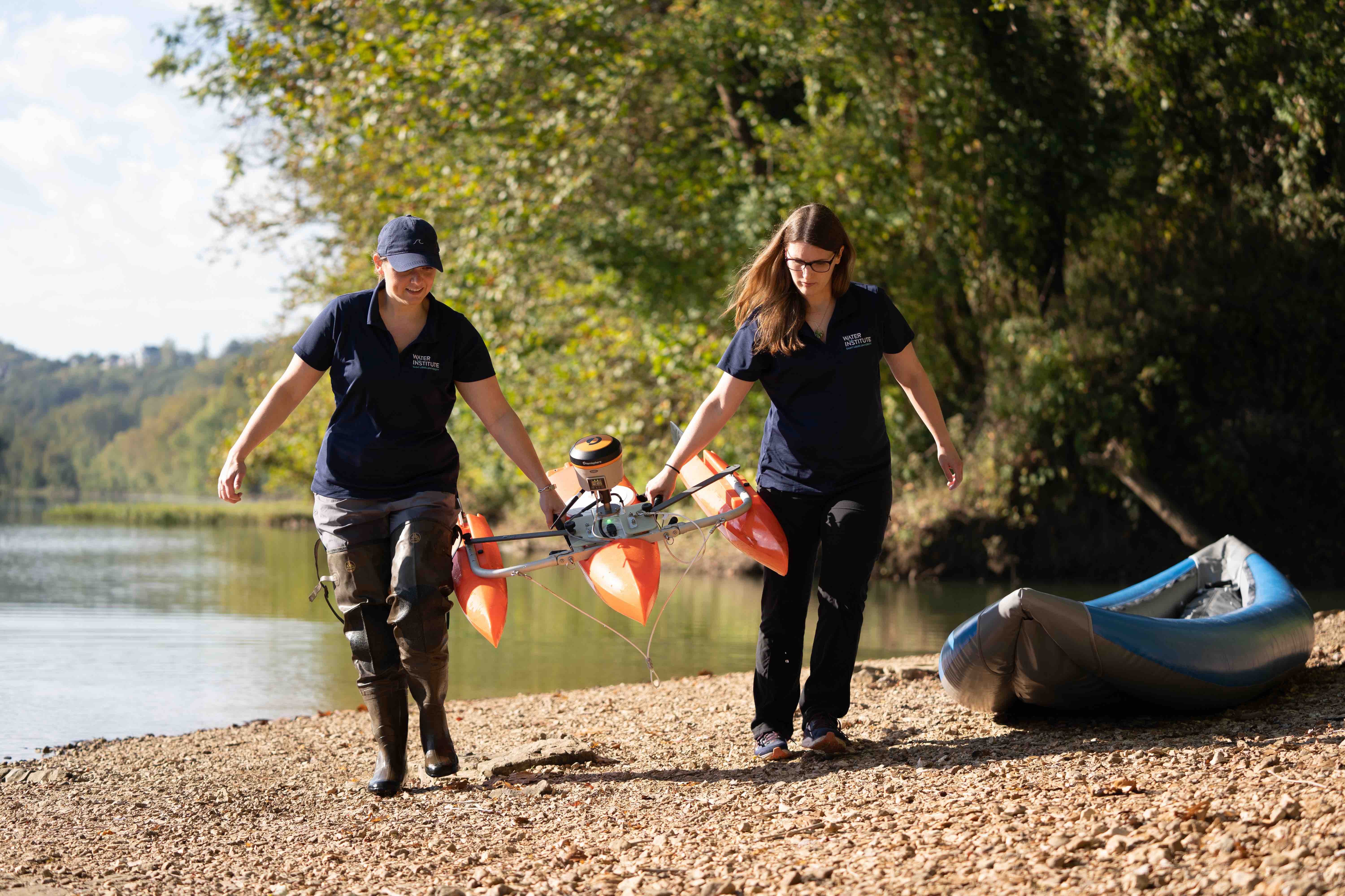 Dr. Amanda Cox and Dr. Liz Hasenmueller carry the ADCP field instrument attached to an orange catamaran flotation device onto the shore after taking data in Meramec River.