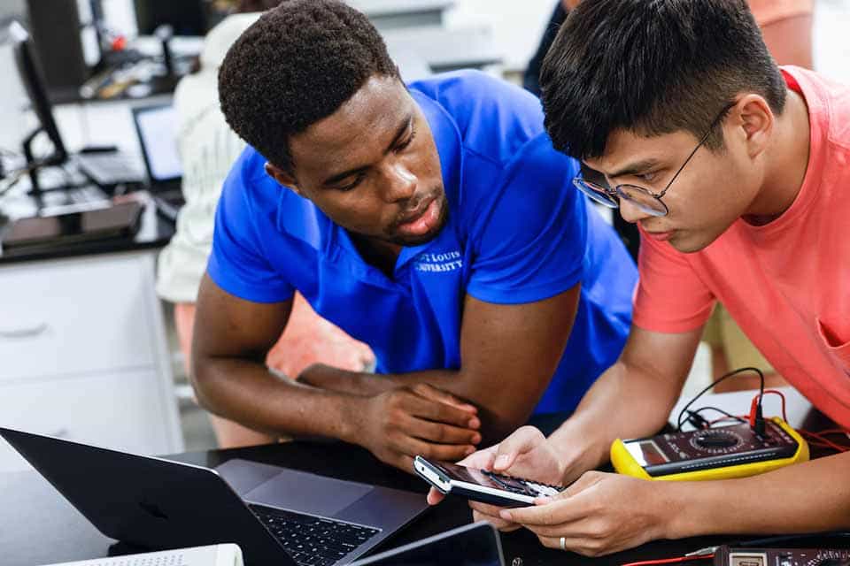 Two male students look at a calculator while working on a device in a lab.