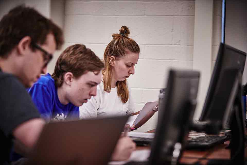 Computer Science students code on laptops in a classroom of the ISS building.