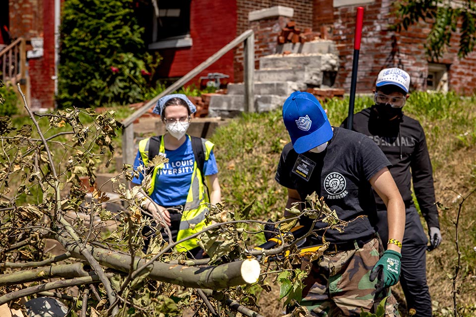 Alumni Take Action After the Disaster Alumni in safety gear walk down a St. Louis street picking up branches